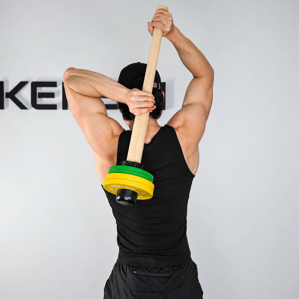 Athlete holding the wooden EZ Clace behind his back with green and yellow weight plates