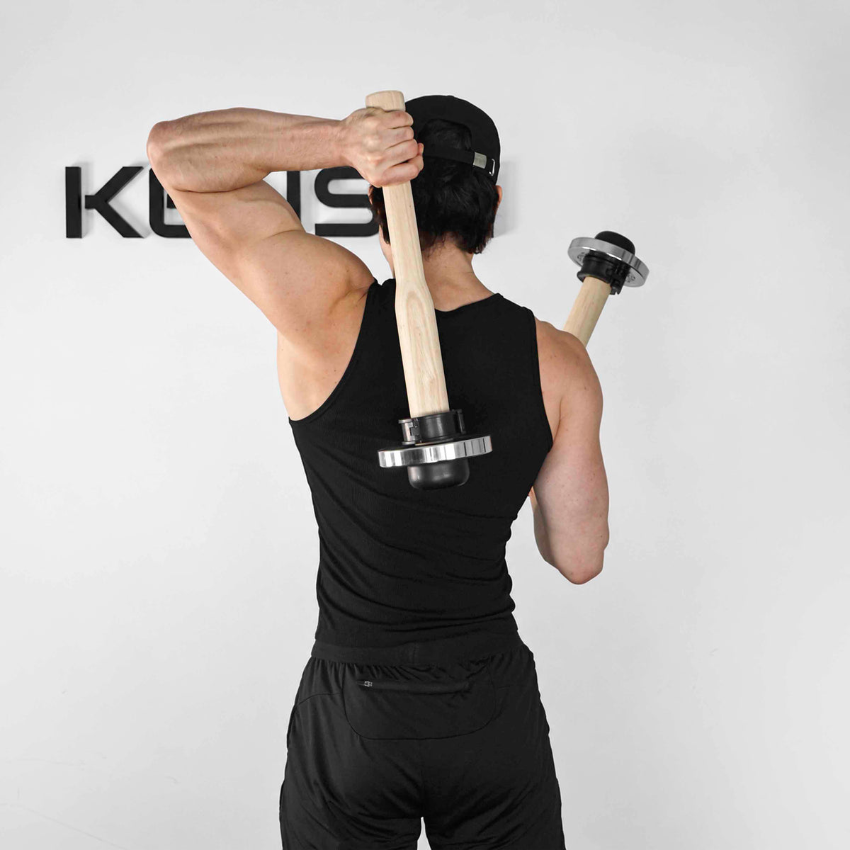 Rear view of an athlete demonstrating an offset swing position with a pair of wooden EZ-CLUB PRO clubs.