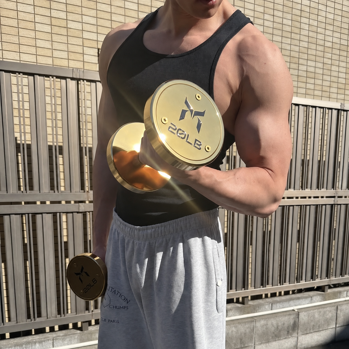 Man performing a biceps curl with gold 20 lb dumbbells outdoors.