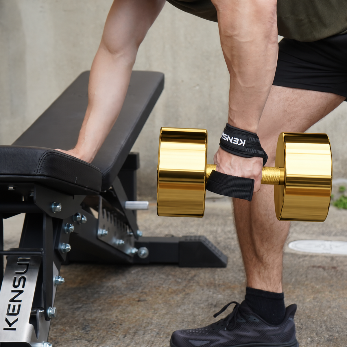 Athlete holding a polished gold dumbbell in a bench-supported row position with Kensui lifting straps