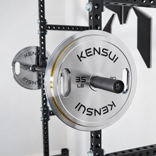 Load image into Gallery viewer, Kensui chrome grip calibrated plates on a barbell in a power rack, showing the 35 LB plate and yellow rim stripe.