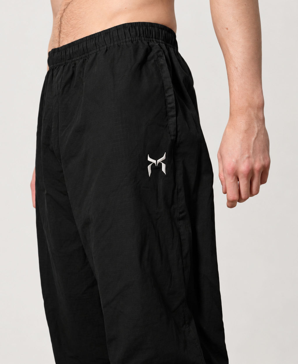 Black cotton pant, side detail showing the elastic waistband, side pocket and white logo.
