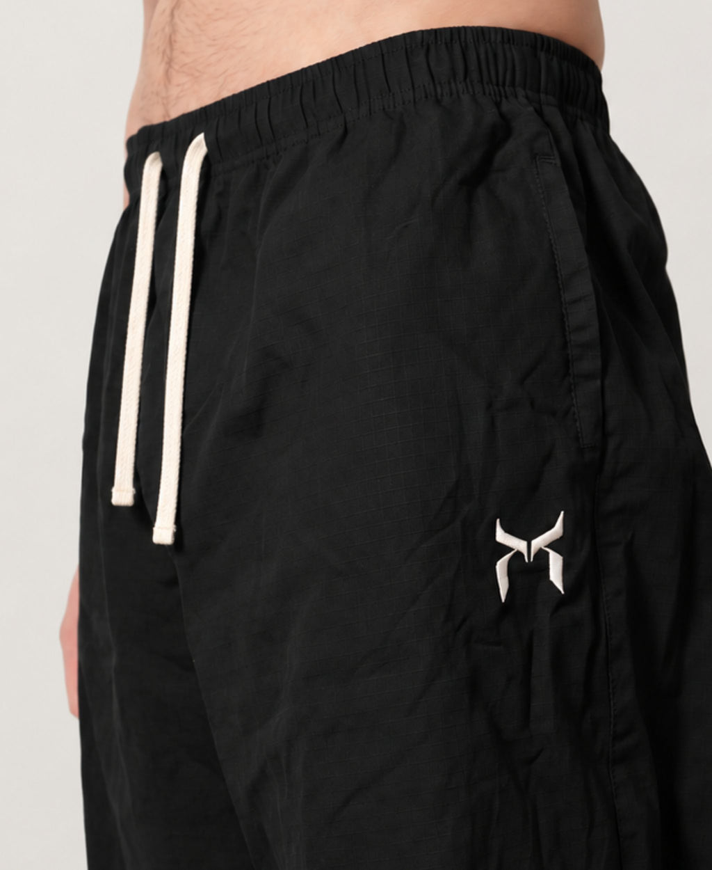 Black cotton pant, close-up of the elastic waistband, drawstrings and white logo.