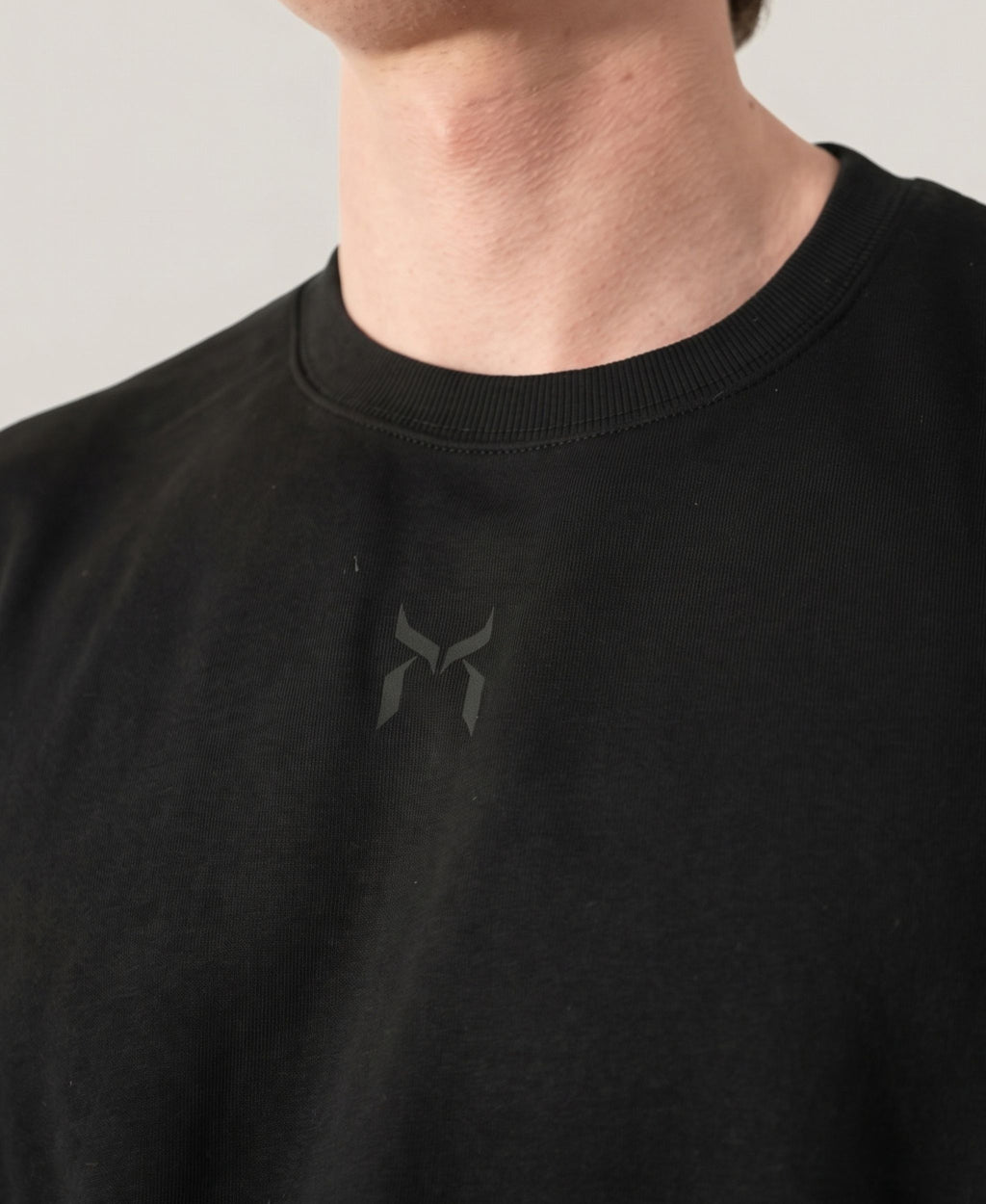 Nanakoribi Crew in black, close-up of the chest logo and ribbed neckline.