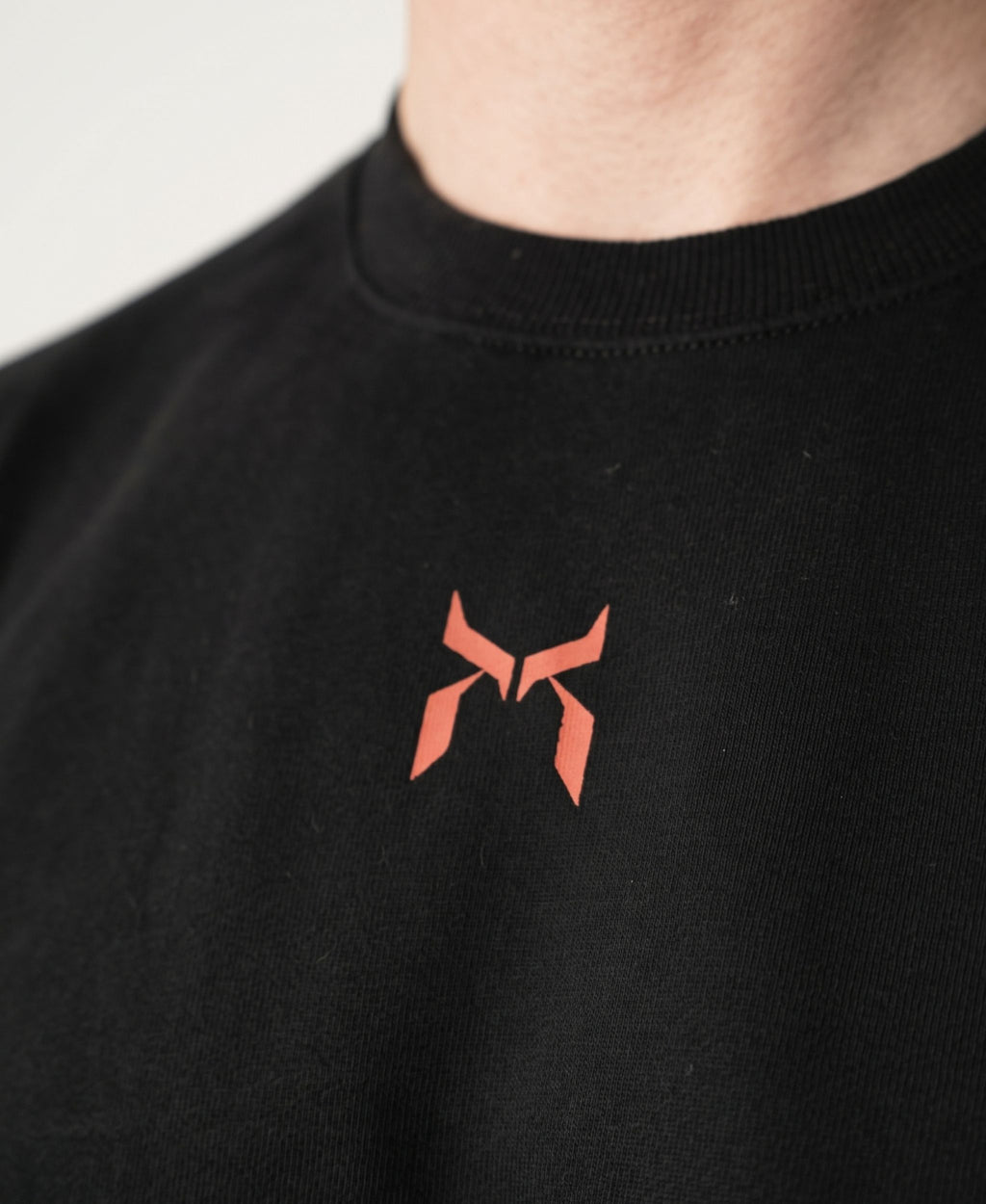 Nanakoribi Crew in black with red print, close-up of the chest logo and ribbed neckline.