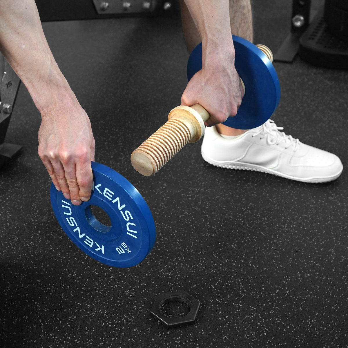 Loading a blue weight plate onto the Timber wooden dumbbell sleeve