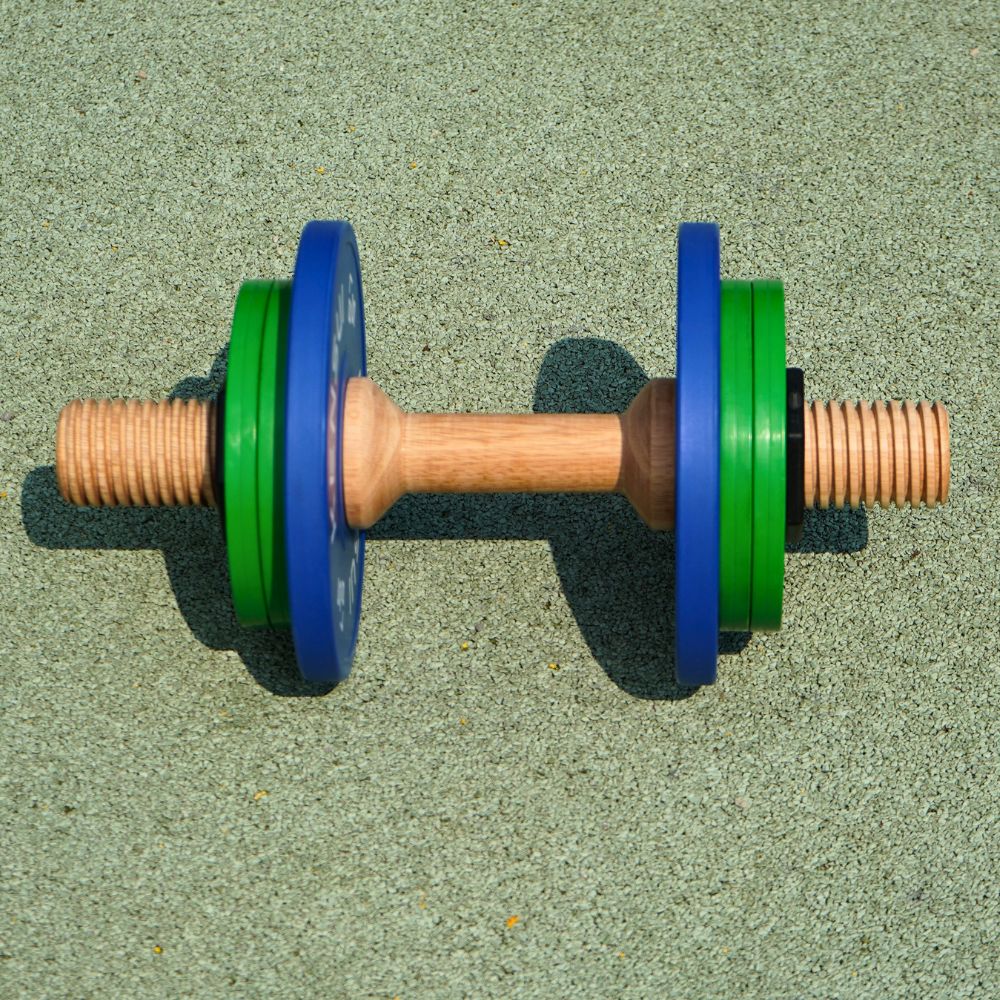 Side view of a Timber wooden dumbbell prototype with blue and green plates