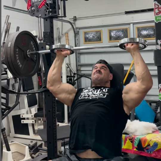 Person pressing a loaded barbell in a home gym.