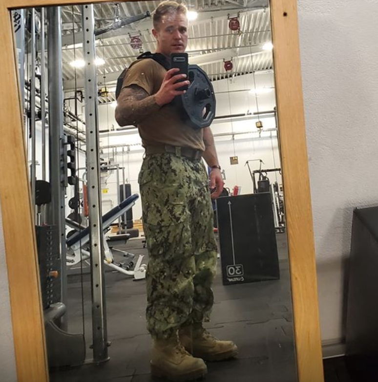 Person in military trousers wearing a weighted vest in a gym.