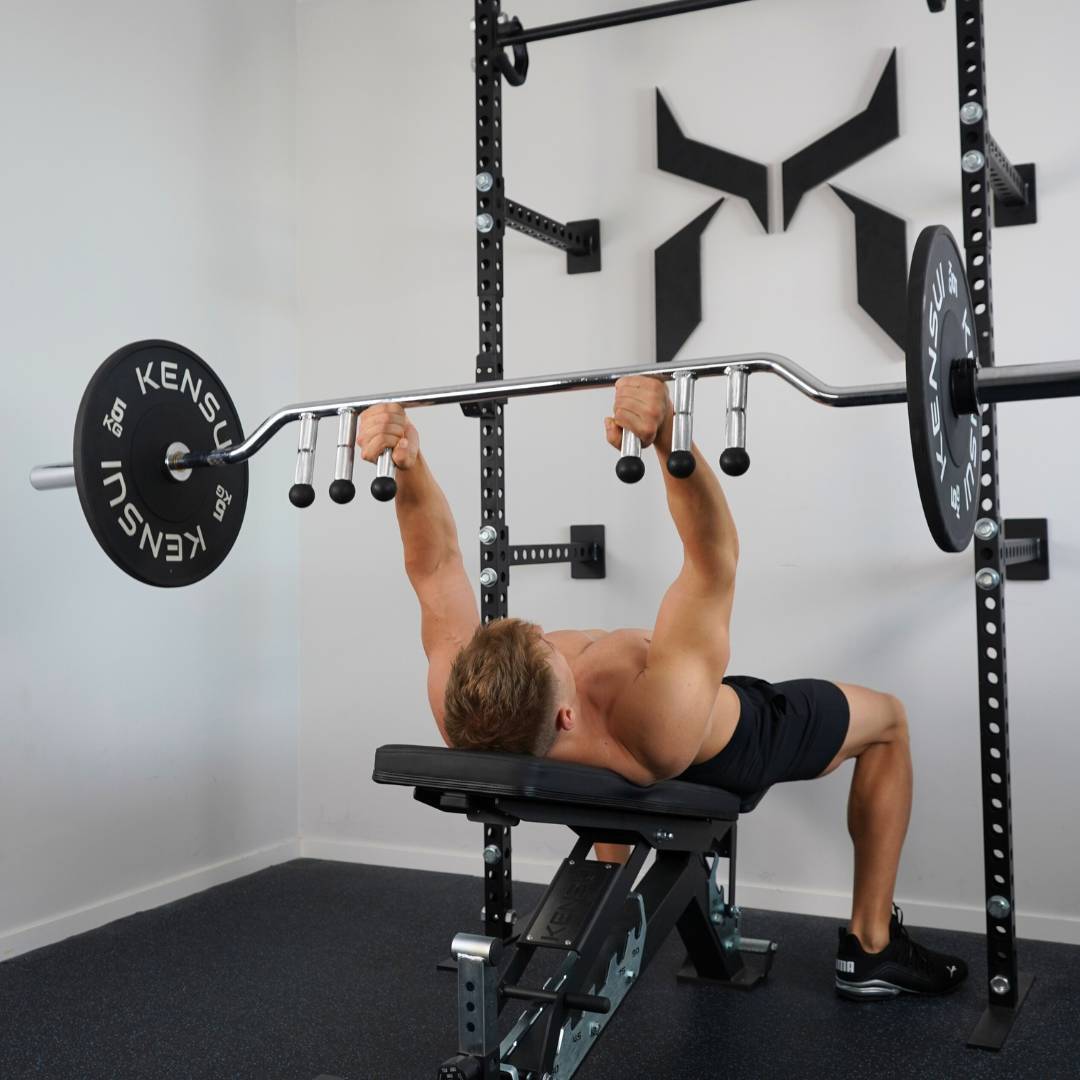 Man bench pressing a barbell while lying on a Kensui adjustable bench.